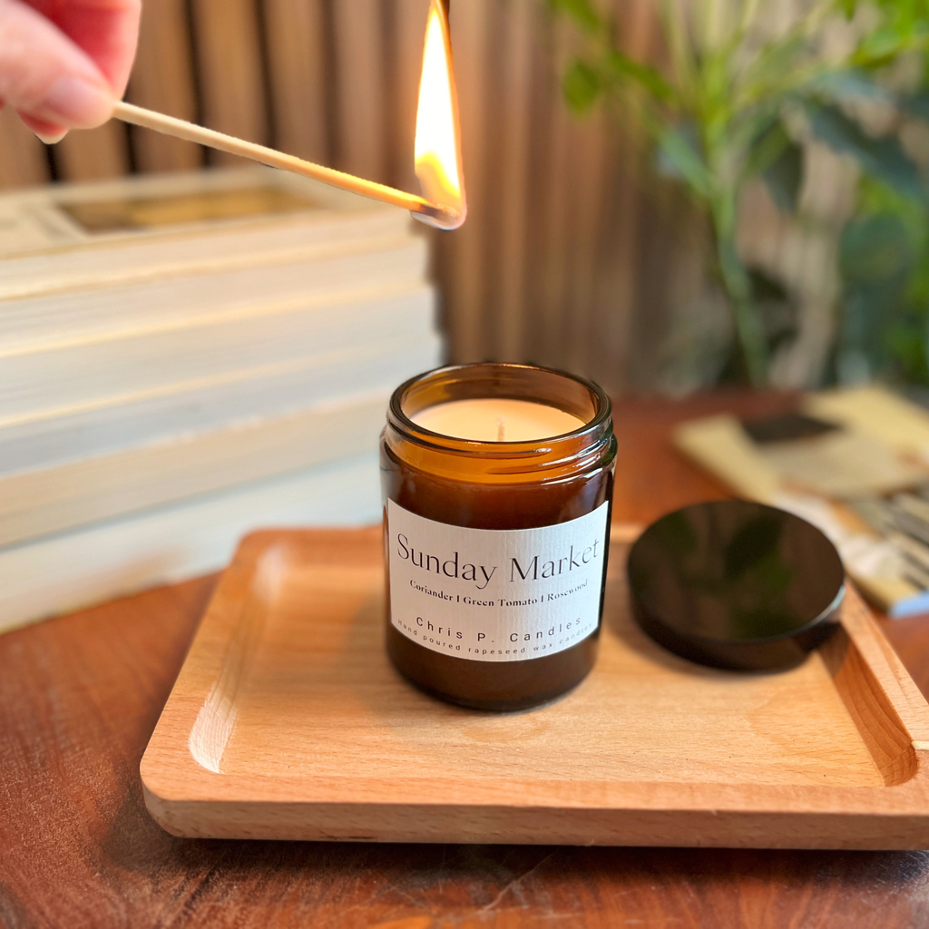 Die Sunday Market Duftkerze im Glas von Chris P. Candles steht auf einem Tisch und verbreitet würzigen Koriander, grüne Tomate und Rosenholz für ein frisches, gemütliches Ambiente.