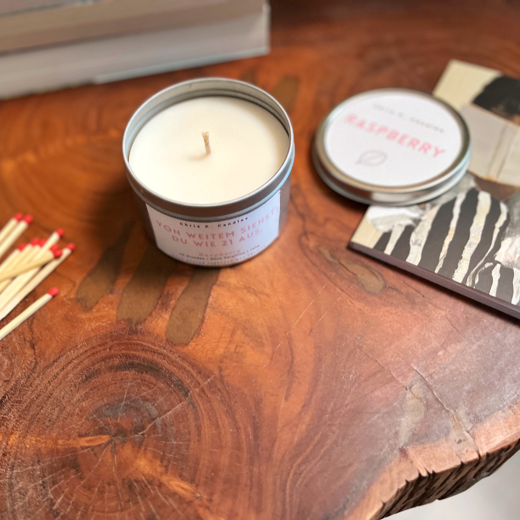 Raspberry-Duftkerze auf Tisch neben Notizbuch und Streichhölzern, handgemacht, vegan, Rapswachs, fruchtiger Himbeerduft für konzentrierte Arbeits- oder Kreativmomente, mit witzigem Spruch ‚Von weitem siehst du wie 21 aus.‘, Geschenkidee für Freundin zum Geburtstag, dekorative Home-Deko.