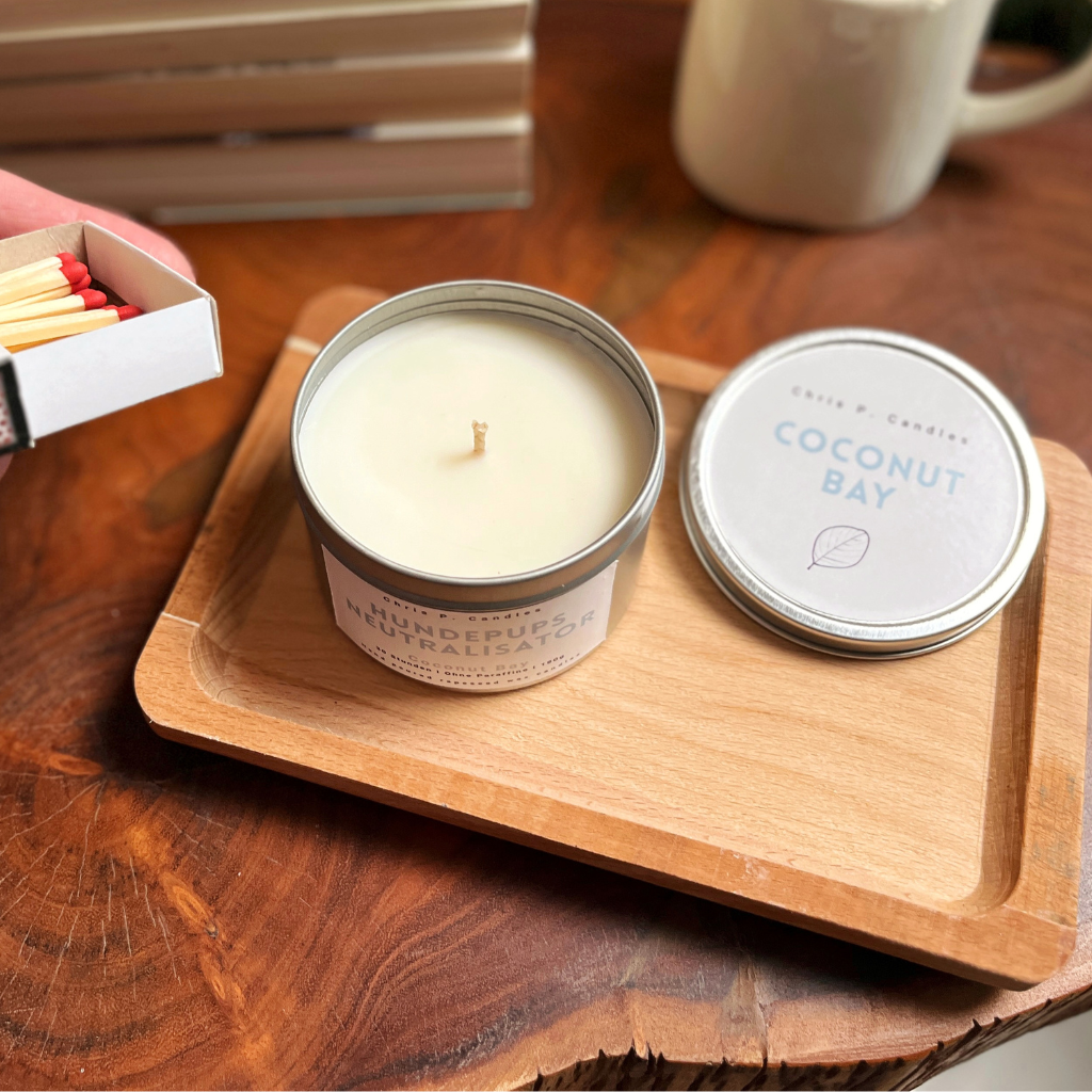 Handgegossene Duftkerze in Dose ‚Hundepups Neutralisator‘ auf Holztisch, vegan aus Rapswachs, Kokosnussduft, humorvolles Design, sorgt für gemütliche Stimmung zuhause.